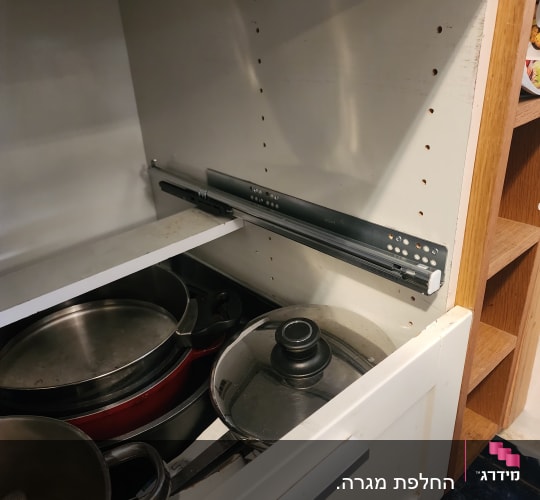 מגירת מטבח פתוחה עם סירים ומכסים
